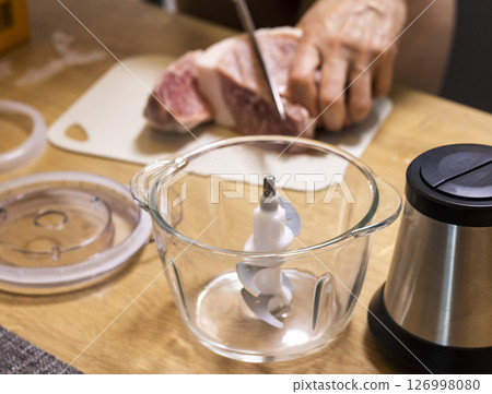 Woman cuts the meat, prepares it to grind it in electrical chopper Woman cuts the meat, prepares it to grind it in electrical chopper 126998080
