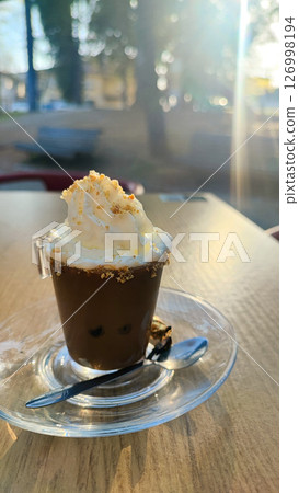 Espresso in a small transparent glass with a mound of cream on top and a sprinkle of cookies against the background of a park. The concept of rest, coffee break, relaxation, coffee business. 126998194
