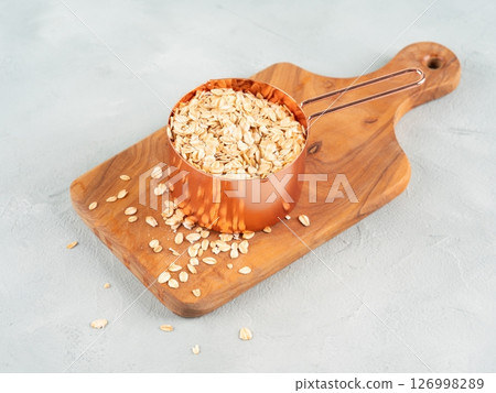Rolled oats in measuring cup on wooden board 126998289