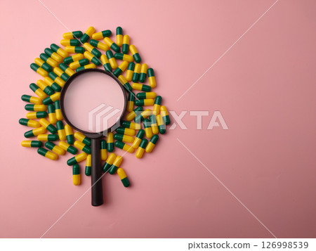 Medicine pill and magnifying glass on a pink background with copy space. Medicine pill and magnifying glass on a pink background with copy space. 126998539