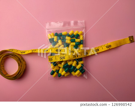 Top view of a medicine pill package with measuring tape on a pink background. 126998542