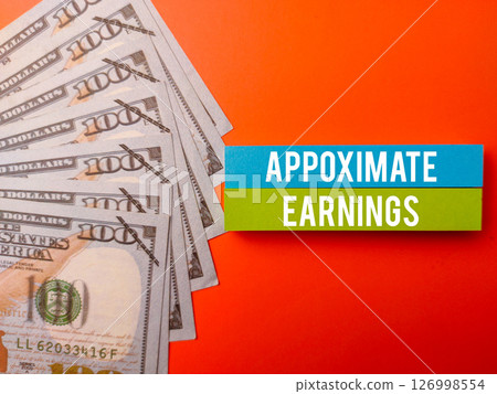 Top view sticky note and banknotes with the word APPOXIMATE EARNINGS on a orange background. 126998554