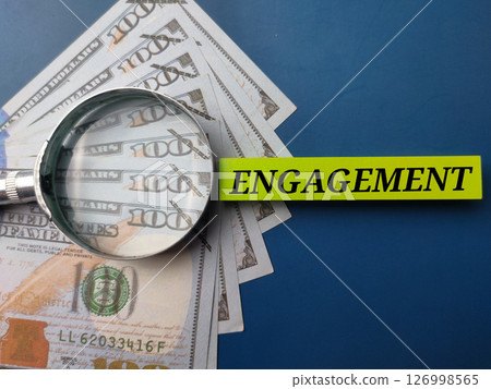Banknotes and magnifying glass with the word ENGAGEMENT on a blue background. 126998565