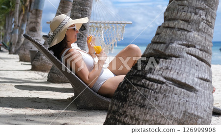 Woman enjoys mango shake on sunbed under palm trees on tropical beach 126999908