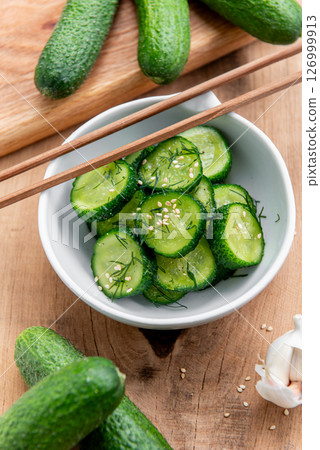 Cucumber salad. Cucumbers slices in a ceramic white bowl on a wooden table. 126999913