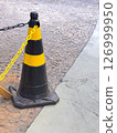 Black and yellow traffic cone on urban cobblestone pavement and concrete sidewalk corner Black and yellow traffic cone on urban cobblestone pavement and concrete sidewalk corner 126999950