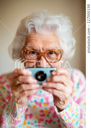 Elderly woman with white hair capturing memories with a camera in a cozy indoor setting during daylight 127000198