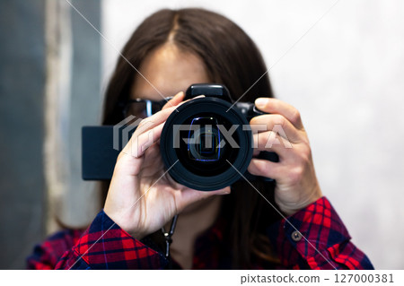 A woman is wearing a plaid shirt and is taking a picture using a camera A woman is wearing a plaid shirt and is taking a picture using a camera 127000381