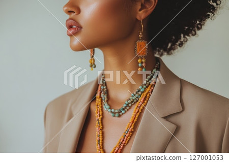 Beautiful woman displaying vibrant jewelry in a stylish outfit against a neutral background during a bright indoor setting 127001053