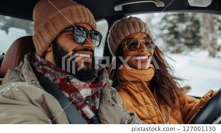 Couple enjoying a winter road trip in a car surrounded by snow-covered trees during a sunny day 127001130