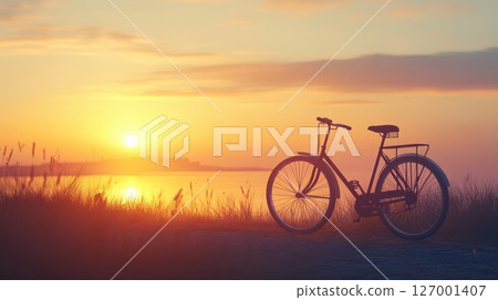 Sunset over the water with a bicycle parked on a grassy path outlining a beautiful evening scene 127001407