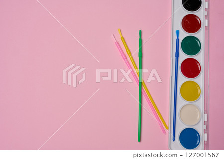 A set of watercolor paints in a plastic case with multi-colored brushes is located on a pink background. A set of watercolor paints in a plastic case with multi-colored brushes is located on a pink background. 127001567