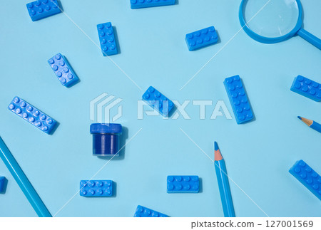 Scattered blue building bricks, pencils, and paint jar on a light blue background. Monochrome creative play, art, or education concept 127001569