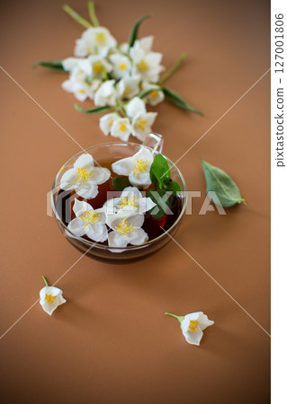 Jasmine and green tea in a transparent teapot close-up on a brown background 127001806