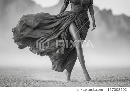 A woman in a long dress is walking on a sandy beach 127002502