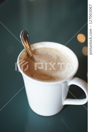 Coffee cup with frothy surface and silver spoon during breakfast Coffee cup with frothy surface and silver spoon during breakfast 127003067