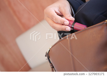 A person is retrieving a lipstick from a stylish handbag while seated A person is retrieving a lipstick from a stylish handbag while seated 127003171