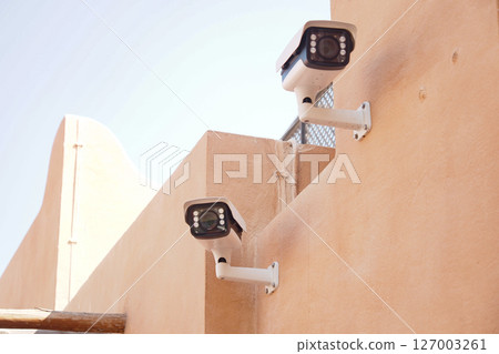 Security cameras mounted on a stucco wall in bright sunlight 127003261