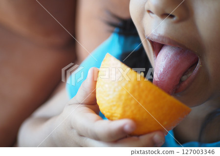 Child enjoying a slice of orange with delight 127003346