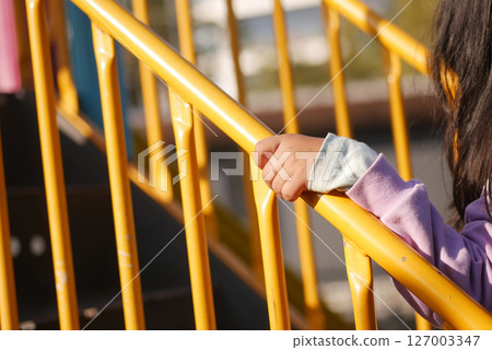 Child grips yellow railing at playground afternoon 127003347