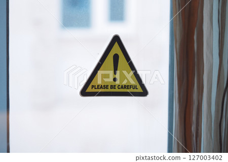 Warning sign urging caution near a window 127003402