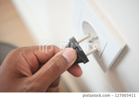 Hand inserting plug into electrical outlet in a home 127003411