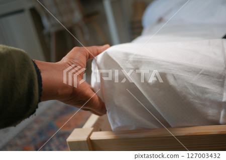 Hand adjusting white bedding on a wooden bed frame 127003432