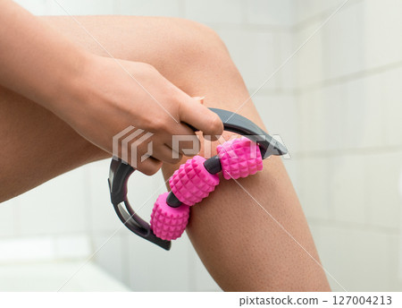 Close-up of a woman massaging her thigh with a pink spiked roller for lymphatic drainage and muscle tension relief	 127004213