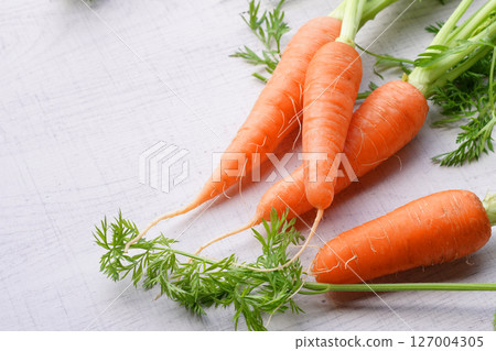 Organic mini carrots with leaves isolated on white wood background. Organic mini carrots with leaves isolated on white wood background. 127004305