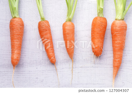 Organic mini carrots with leaves isolated on white wood background. Organic mini carrots with leaves isolated on white wood background. 127004307