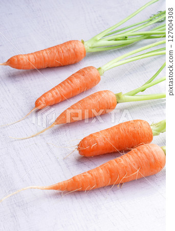 Organic mini carrots with leaves isolated on white wood background. Organic mini carrots with leaves isolated on white wood background. 127004308