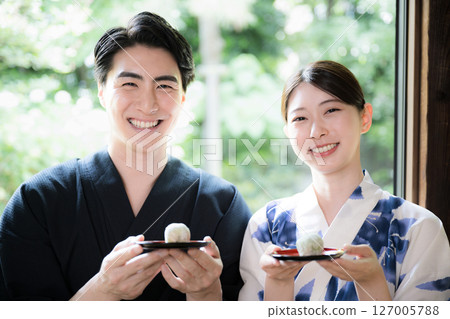穿著浴衣的男女在陽台上吃饅頭和日本糖果,旅館或客棧的旅行照片,看著鏡頭 穿著浴衣的男女在陽台上吃饅頭和日本糖果,旅館或客棧的旅行照片,看著鏡頭 127005788