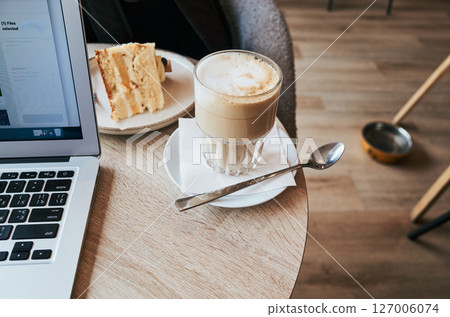 Laptop is on a table with a cake and a cup of coffee 127006074