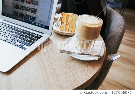 Laptop is on a table with a cake and a cup of coffee Laptop is on a table with a cake and a cup of coffee 127006075