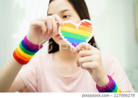 Asian woman holding LGBT heart with rainbow flag. Asian woman holding LGBT heart with rainbow flag. 127006279