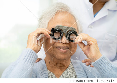 Optometrist checking Asian elderly woman ophthalmic vision eye test and using optical trial frame. 127006317