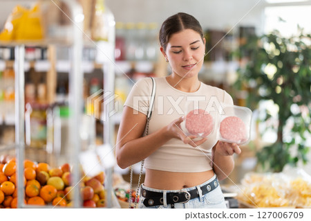 Girl looking at raw hamburger cutlet in store, choose meat ware 127006709
