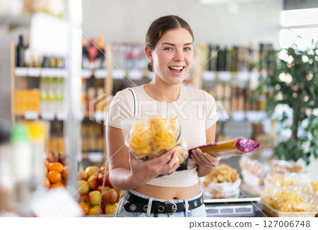 Young woman is holding packages of pasta and spaghetti in hands, choosing food for garnish side dish Young woman is holding packages of pasta and spaghetti in hands, choosing food for garnish side dish 127006748