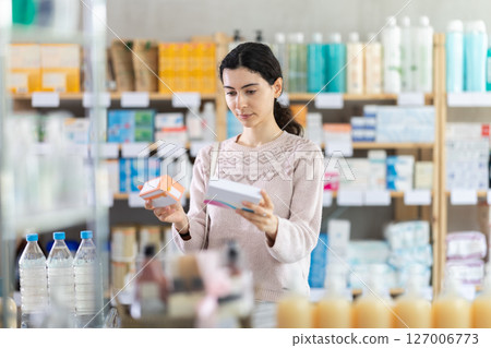 Young woman choosing boxes of pills in pharmacy 127006773