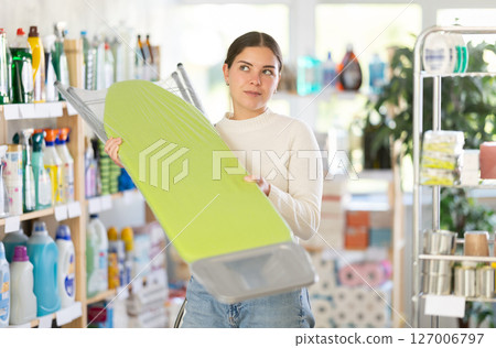 Girl housewife in household store examines goods, chooses ironing board 127006797