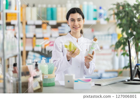 Female pharmacist holding shampoos near counter 127006801