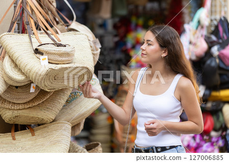 Girl choosing fashionable straw bag with interest at street market Girl choosing fashionable straw bag with interest at street market 127006885