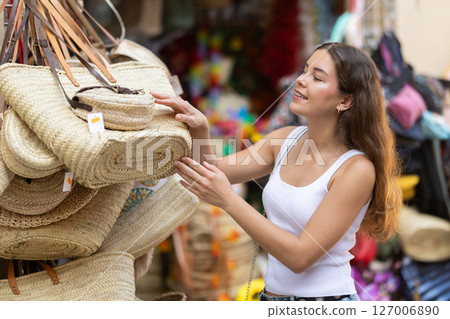 Girl choosing fashionable straw bag with interest at street market 127006890