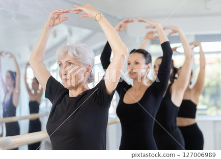 Elderly woman maintaining fifth position during group ballet workout Elderly woman maintaining fifth position during group ballet workout 127006989