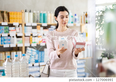 Young woman choosing boxes of pills in pharmacy 127006991