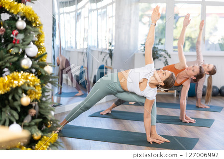 Woman performing Utthita Parsvakonasana in yoga studio decorated with Christmas tree 127006992