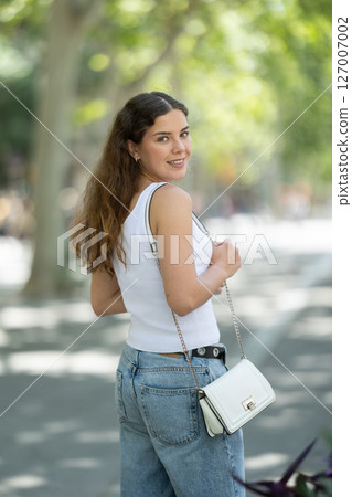 Cheerful girl turning back while walking on sunlit summer city street Cheerful girl turning back while walking on sunlit summer city street 127007002