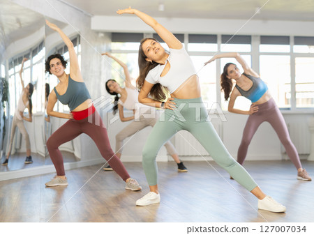 Group of girls in fitness studio performs warm-up, prepares for active dancing and sports. Group of girls in fitness studio performs warm-up, prepares for active dancing and sports. 127007034