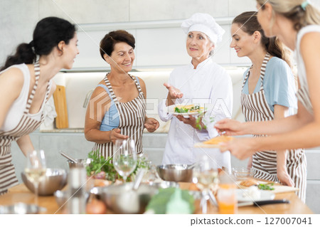 Mature female cook holding plate with cooked chicken Mature female cook holding plate with cooked chicken 127007041