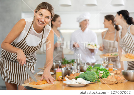 Girl at group class of culinary school cuts up chicken and prepares low-calorie diet lunch Girl at group class of culinary school cuts up chicken and prepares low-calorie diet lunch 127007062